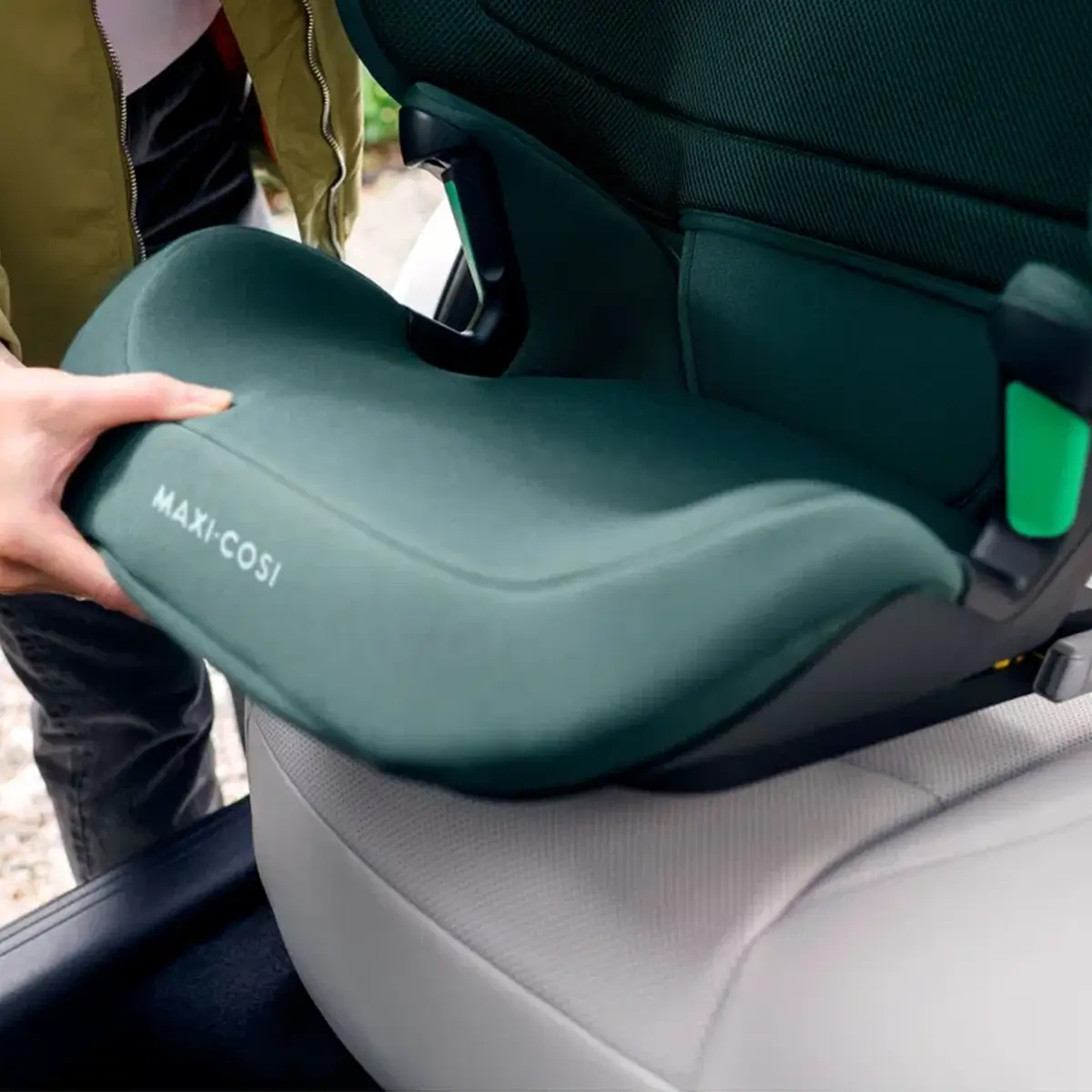 Jemand installiert sorgfältig einen grünen Maxi-Cosi RodiFix R i-Size-Autositz im Fahrzeug.