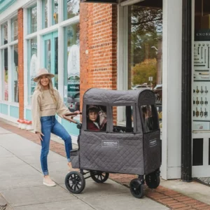 Eine Frau mit Hut schiebt ihre Kinder in einem Wonderfold Bollerwagen mit Cold Weather Shield W4