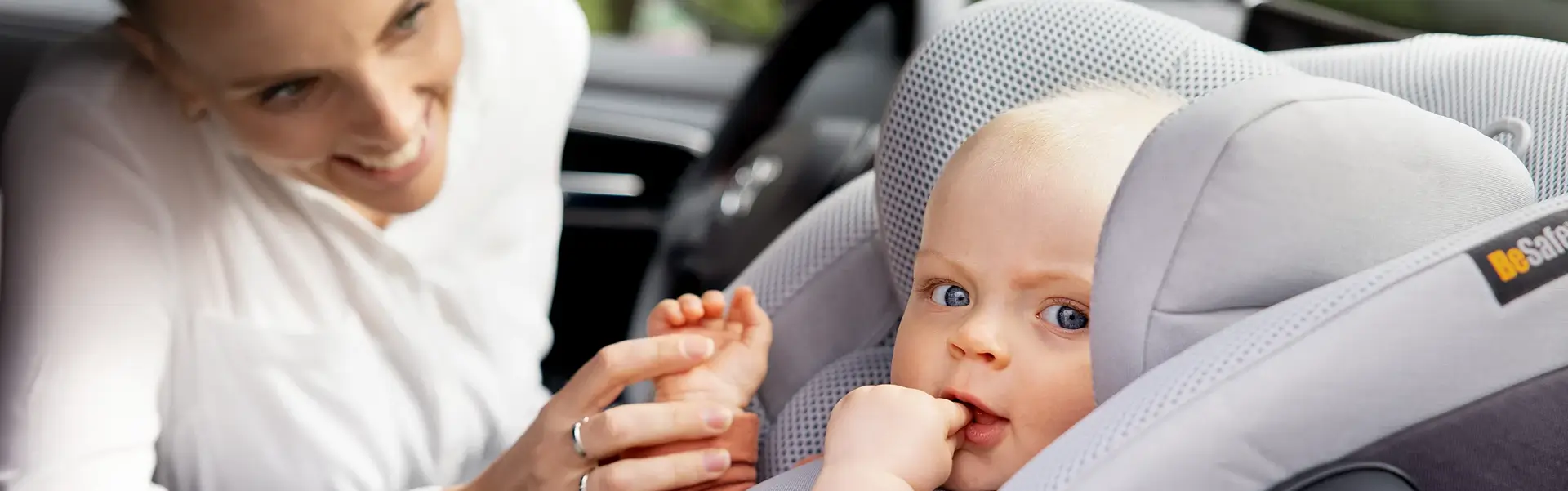 Ein Elternteil lächelt sein Baby im Autositz an. Das Kind nuckelt glücklich an seinen Fingern und blickt in die Kamera, sicher angeschnallt mit der BeSafe iZi Modular i-Size Base. Ein Elternteil lächelt sein Baby im Autositz an. Das Kind nuckelt glücklich an seinen Fingern und blickt in die Kamera, sicher angeschnallt mit der BeSafe iZi Modular i-Size Base.