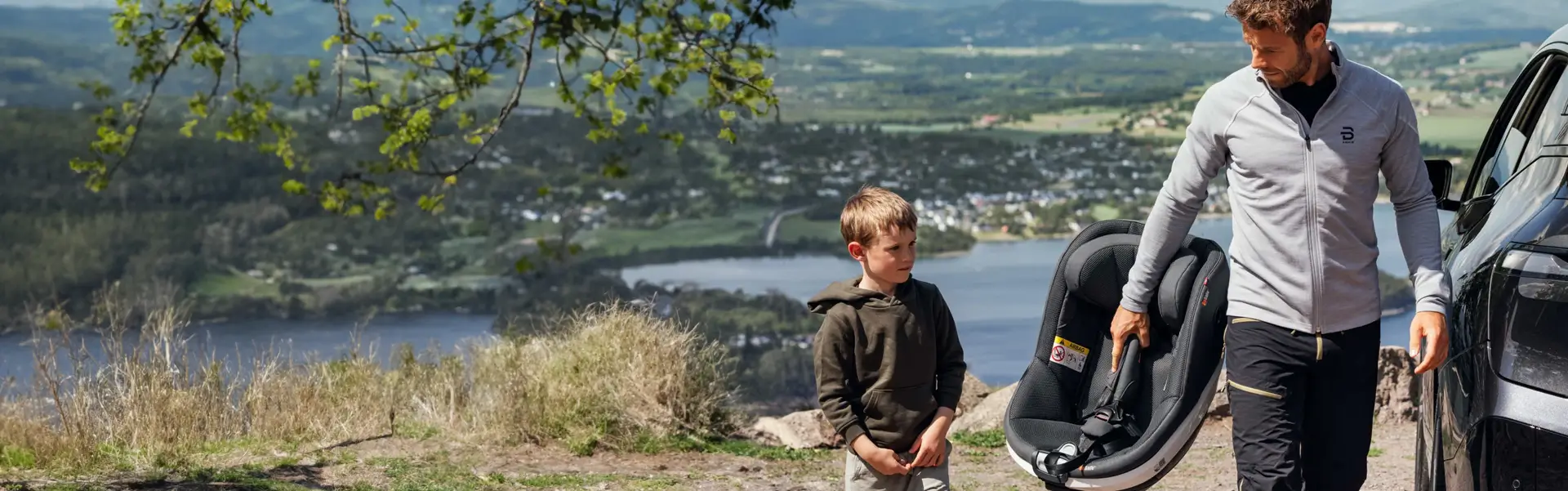 Ein Mann mit einem BeSafe Beyond-Kindersitz steht neben einem Auto mit einem kleinen Jungen. 