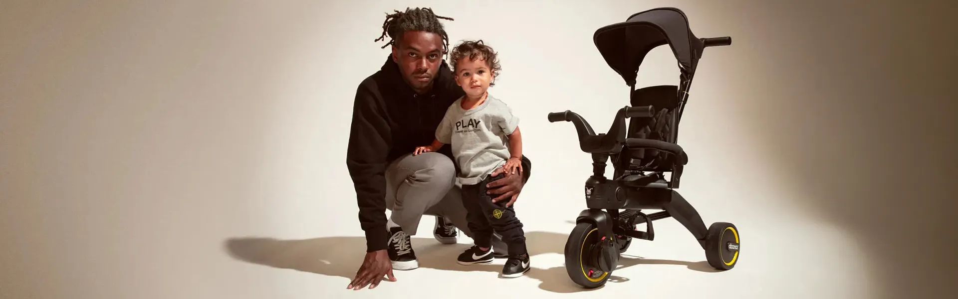 Ein Mann hockt neben einem kleinen Kind und bewundert das schlanke Design des Doona Dreirad Liki Trike S1.