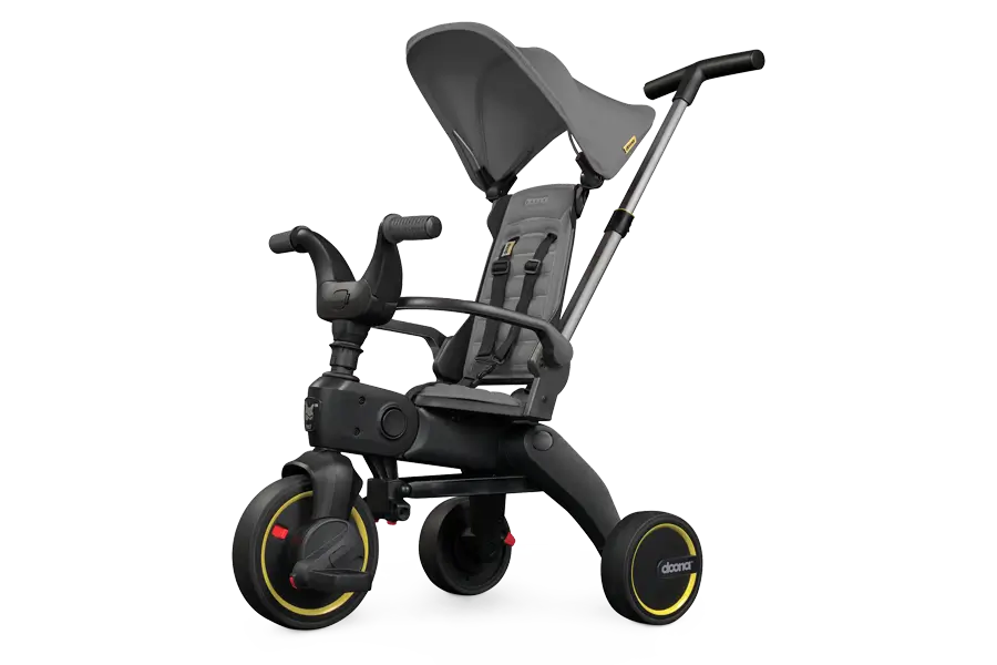 Das Doona Dreirad Liki Trike S1 ist ein elegantes, schwarz-graues, umbaubares Babydreirad mit Verdeck und Lenkstange, drei Rädern und auffälligen gelben Akzenten.