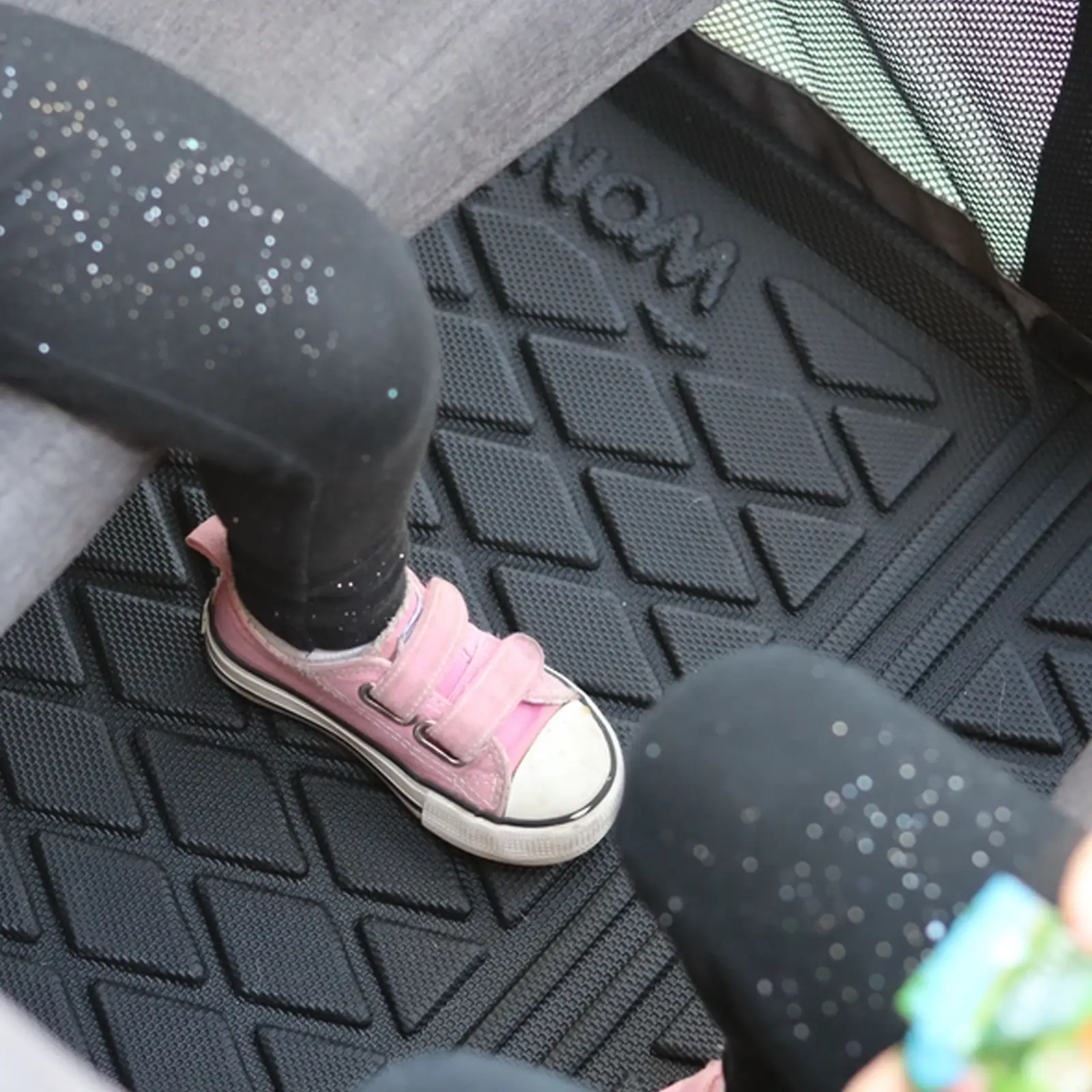 Ein Kind sitzt auf einer Wonderfold Allwetter-Fußmatte mit Strukturmuster.