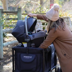 Eine Frau mit Beanie ist draußen und stellt in ihrem Wagen einen Autositz mit dem Wonderfold Autositz-Adapter W2 Serie ein.